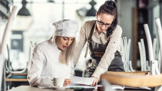 Business owner shows numbers to a surprised chef after hours in the restaurant.