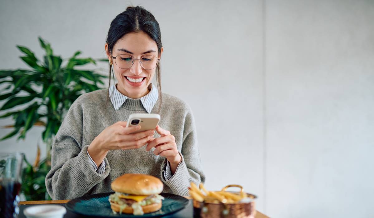 Adobe stock woman at a restaurant taking a picture of her burger.