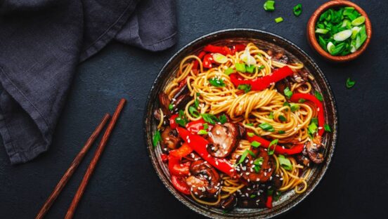 Vegan stir fry egg noodles with vegetables, paprika, mushrooms, chives and sesame seeds in bowl.