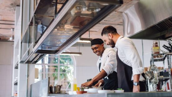 Two cooks preparing food in restaurant kitchen.