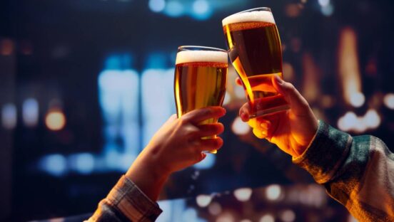 Two glasses of beer being toasted at a bar.