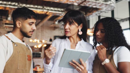 Restaurant manager talking to two employees while holding a tablet.