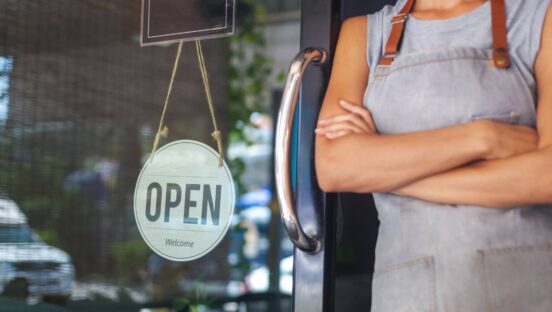 Restaurant owner leaning against window with an open sign.