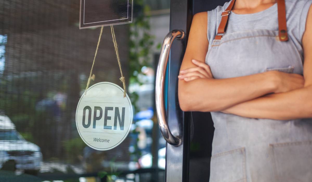 Restaurant owner leaning against window with an open sign.