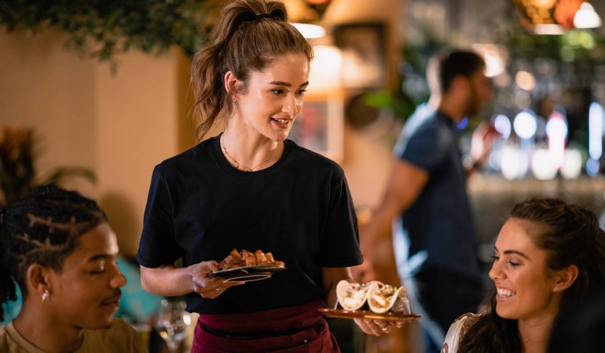Restaurant server handing food to two customers at a table.