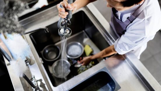 Restaurant employee washing dishes in sink.
