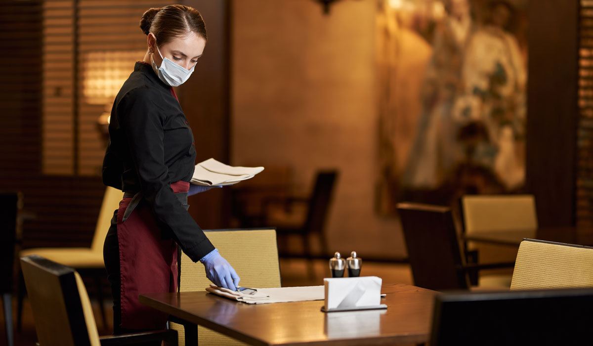 Restaurant Server In Protective Mask Preparing Table