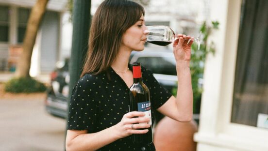 Woman drinking red wine out of a glass while holding the bottle.